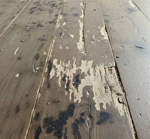 Worn wooden floor with peeling paint and scuffed areas in various shades of brown and black.